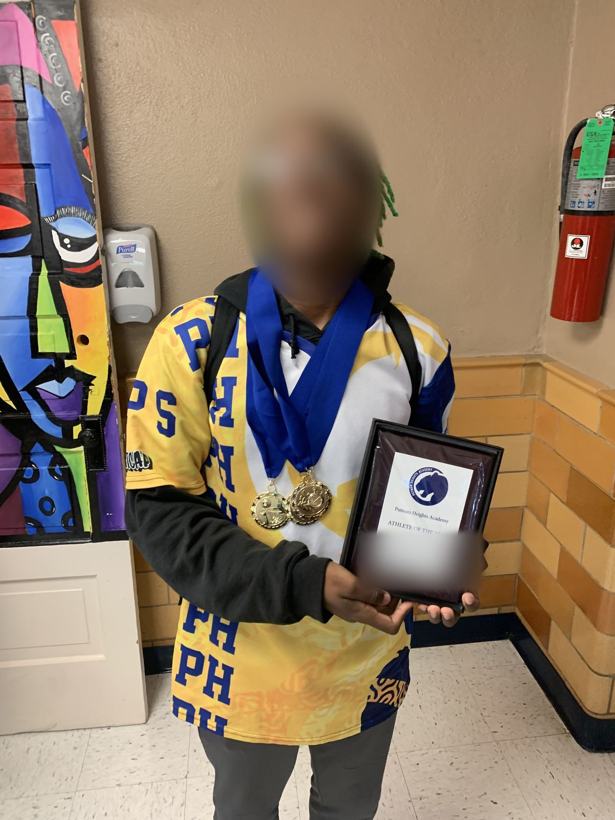 Student athlete in a Putnam Heights jersey with medals and an Athlete of the Year plaque. Face and name blurred.