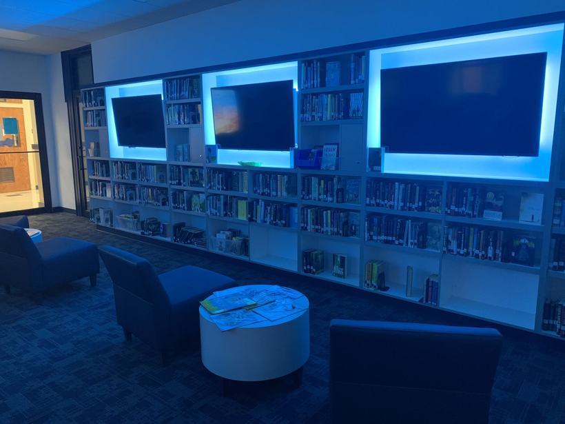 LED-lit library shelf wall with screens and lounge seating.