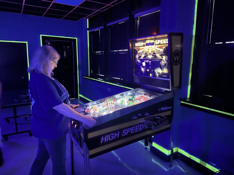 Staff member playing pinball in the blacklit arcade.