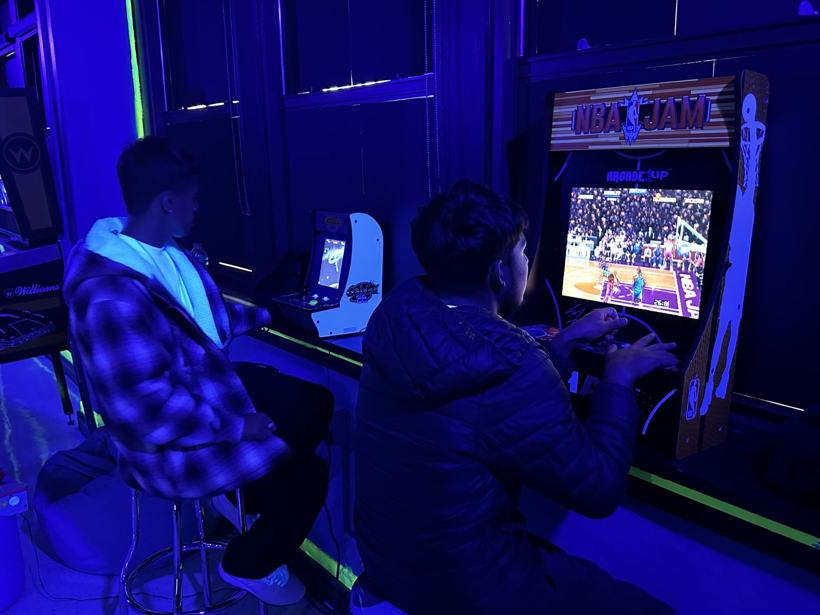 Two students playing NBA Jam, seen from behind.