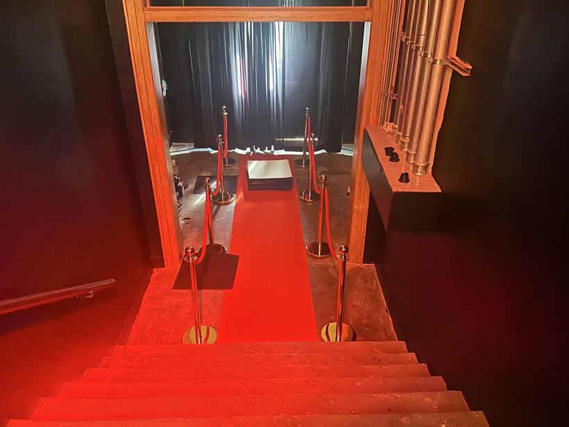 Red carpet and gold stanchions leading to the curtained reveal room.
