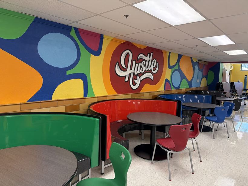 Hustle mural above red, green, and blue cafeteria booths.