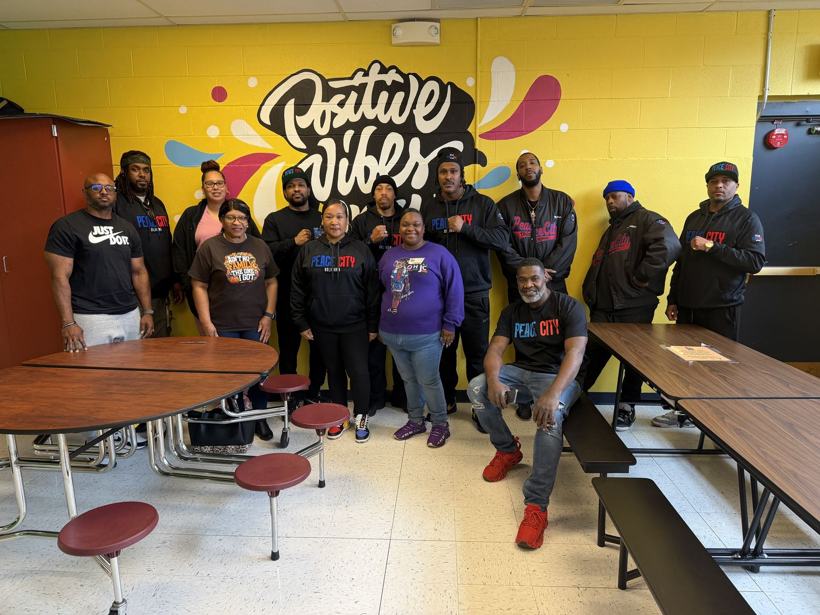 A group of adult mentors from Peace City Oklahoma in front of a mural.