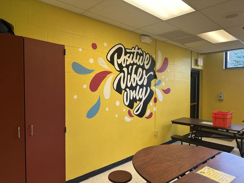 Positive Vibes Only mural on a yellow cafeteria wall.