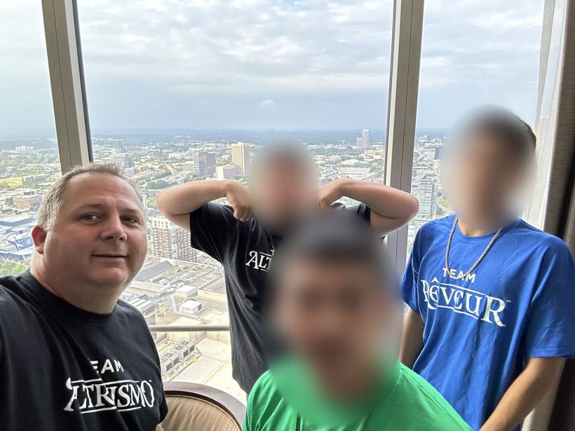 Staff member and students in house shirts at a high-rise hotel window. Student faces blurred.