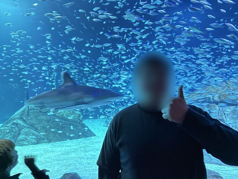 Student giving a thumbs up in front of a shark tank. Face blurred.